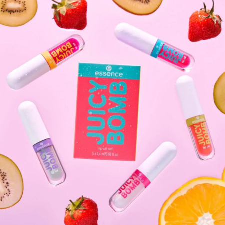 Sur un fond rose, un ensemble d'huiles à lèvres colorées est disposé en cercle autour d'un emballage « Juicy Bomb ». Des fraises coupées en deux, des tranches de kiwi et une orange sont dispersées, rehaussant l'esthétique vibrante et fraîche du produit. Dakar