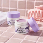 Deux pots ouverts de masque de nuit Essence, avec couvercles violets, posés sur une surface carrelée. Une pince à cheveux rose et une serviette sont visibles à l'arrière-plan. Dakar