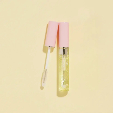 Un brillant à lèvres transparent avec un capuchon rose est ouvert, révélant la baguette applicatrice, sur un fond beige clair. Dakar
