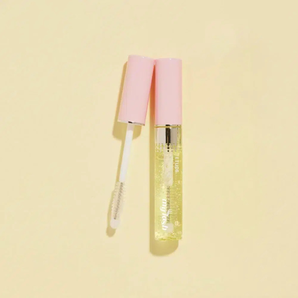 Un brillant à lèvres transparent avec un capuchon rose est ouvert, révélant la baguette applicatrice, sur un fond beige clair. Dakar