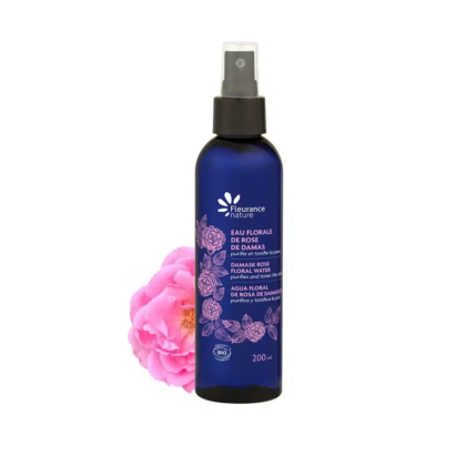 Un vaporisateur bleu foncé, étiqueté « Eau Florale de Rose de Damas », aux motifs floraux roses, trône à côté d'une rose rose en fleurs. Ce flacon, produit par Fleurance Nature, contient 200 ml d'Eau Florale de Rose de Damas. Dakar