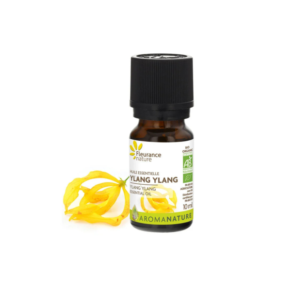 Un petit flacon marron d'huile essentielle d'ylang-ylang Fleurance Nature avec un bouchon noir. L'étiquette est blanche avec des détails jaunes et verts. Des pétales de fleurs d'ylang-ylang jaunes sont disposés à côté du flacon. Le flacon contient 10 ml. Dakar
