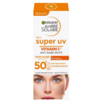 Emballage de la crème solaire Garnier Ambre Solaire Super UV, enrichie en vitamine C et anti-taches. Elle revendique une protection SPF 50+ très élevée. La boîte représente un visage de femme et un gros plan sur le grain de peau. Texte principalement en allemand. Dakar
