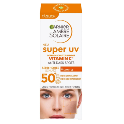 Emballage de la crème solaire Garnier Ambre Solaire Super UV, enrichie en vitamine C et anti-taches. Elle revendique une protection SPF 50+ très élevée. La boîte représente un visage de femme et un gros plan sur le grain de peau. Texte principalement en allemand. Dakar