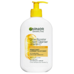 Un flacon blanc de crème nettoyante Garnier SkinActive Glow Booster à la vitamine C. L'étiquette présente des touches d'orange et une tranche d'orange. Le flacon pompe est jaune. Le texte souligne ses bienfaits nettoyants et hydratants. Dakar