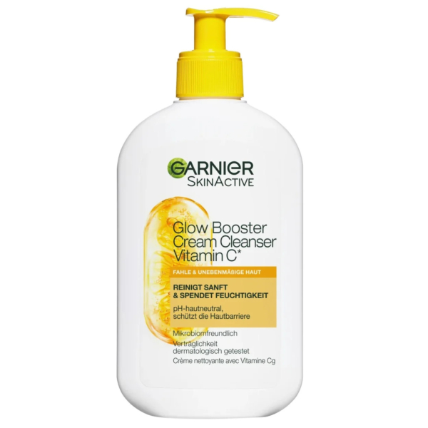 Un flacon blanc de crème nettoyante Garnier SkinActive Glow Booster à la vitamine C. L'étiquette présente des touches d'orange et une tranche d'orange. Le flacon pompe est jaune. Le texte souligne ses bienfaits nettoyants et hydratants. Dakar