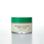 Un pot de crème éclat correctrice anti-taches AXIS-Y avec un couvercle vert. L'étiquette est de couleur crème et indique le nom du produit et son contenu : 50 ml (1,69 fl.oz), avec de petits détails graphiques et des logos. Dakar
