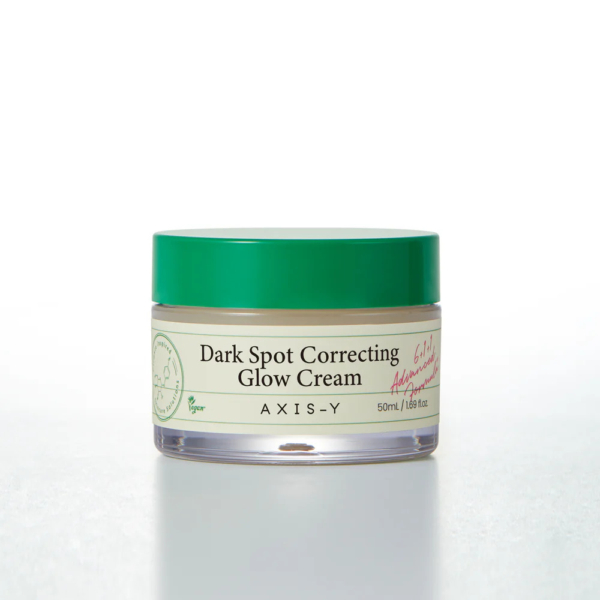 Un pot de crème éclat correctrice anti-taches AXIS-Y avec un couvercle vert. L'étiquette est de couleur crème et indique le nom du produit et son contenu : 50 ml (1,69 fl.oz), avec de petits détails graphiques et des logos. Dakar