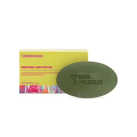 Un pain de savon ovale vert, gravé « Good Molecules », est placé devant une boîte jaune. Cette dernière est ornée d'un motif abstrait coloré et porte l'inscription « Brightening & Dark Spots Bar » (Barre éclaircissante et anti-taches brunes) ainsi que les informations produit. Dakar