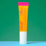 Un tube jaune vif de sérum à la vitamine C Good Molecules avec Orizanol se dresse sur un fond vert et bleu. Le bouchon est magenta et le nom du produit est imprimé verticalement en rouge. Dakar