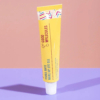 Un tube jaune de gel contour des yeux Yerba Maté Wake Up de Good Molecules sur une surface rose. Le tube présente des touches géométriques colorées et projette une ombre. Dakar