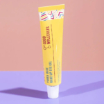 Un tube jaune de gel contour des yeux Yerba Maté Wake Up de Good Molecules sur une surface rose. Le tube présente des touches géométriques colorées et projette une ombre. Dakar