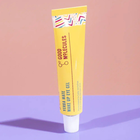 Un tube jaune de gel contour des yeux Yerba Maté Wake Up de Good Molecules sur une surface rose. Le tube présente des touches géométriques colorées et projette une ombre. Dakar