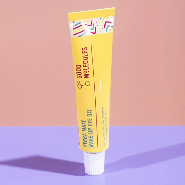 Un tube jaune de gel contour des yeux Yerba Maté Wake Up de Good Molecules sur une surface rose. Le tube présente des touches géométriques colorées et projette une ombre. Dakar