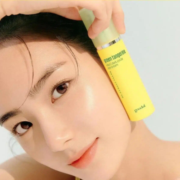 Une personne tient un tube jaune de produit de soin étiqueté « mandarine verte » à côté de son visage, affichant une peau lisse et éclatante. L'arrière-plan est un doux dégradé de blanc et de bleu clair. Dakar