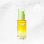 Un flacon de sérum anti-taches Goodal Green Tangerine à la vitamine C est présenté sur un fond clair et texturé. Le flacon est jaune, avec un bouchon vert et un texte blanc. Dakar
