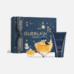Un coffret cadeau Guerlain Shalimar décoratif comprend deux flacons de parfum dorés et un tube de lotion bleu foncé. Le coffret bleu marine est orné de motifs célestes dorés et du logo « Guerlain Paris ». Dakar