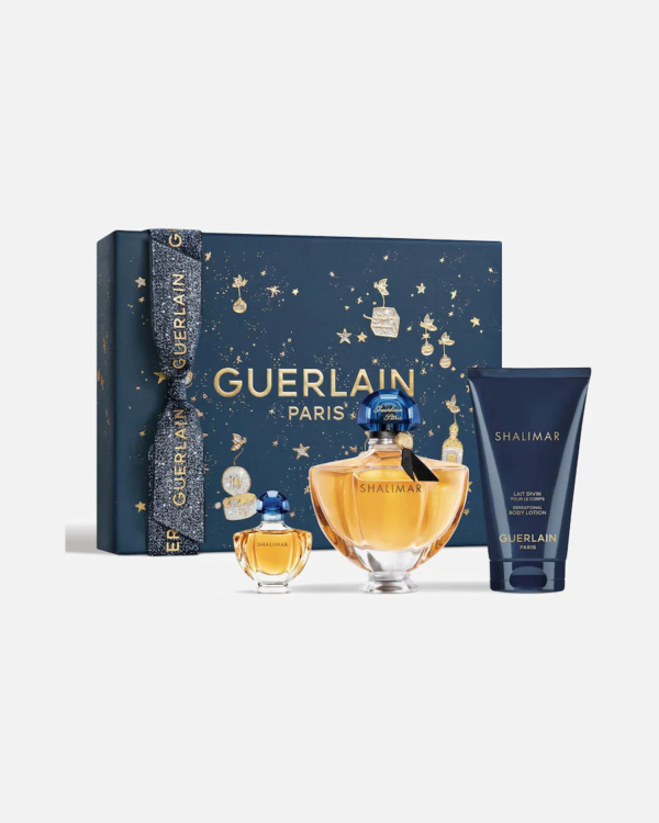 Un coffret cadeau Guerlain Shalimar décoratif comprend deux flacons de parfum dorés et un tube de lotion bleu foncé. Le coffret bleu marine est orné de motifs célestes dorés et du logo « Guerlain Paris ». Dakar