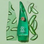 Un flacon vert de gel apaisant Holika Holika Aloe 99 % est posé sur un fond vert, entouré de tranches d'aloe vera fraîches. Des gouttes d'eau apportent une touche rafraîchissante. Dakar