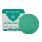 Image d'un emballage de savon Topsygel et d'un pain de savon rond vert. L'emballage est blanc avec des touches de vert et un texte en français, soulignant ses propriétés clarifiantes et éclaircissantes pour le visage et le corps. Dakar