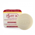 Un savon nettoyant rond couleur ivoire, estampillé « HT26 Paris », est présenté devant une boîte assortie. L'emballage porte l'inscription « Savon Nettoyant Purifiant » en français et en anglais, avec des touches de rouge et des détails dorés. Dakar