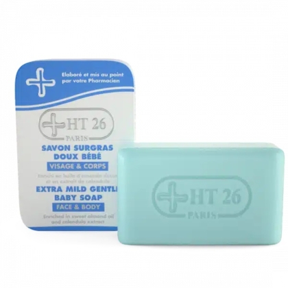 Un pain de savon rectangulaire bleu à côté de son emballage. L'emballage est blanc et bleu, avec des inscriptions en français et en anglais, notamment « HT 26 » et « Savon bébé extra doux visage et corps ». Une croix médicale figure dans le coin supérieur gauche. Dakar