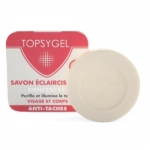Barre de savon ronde beige devant une boîte rectangulaire rouge et blanche avec un dessin et un texte, incluant les mots « Topsygel » et « Savon Éclaircissant ». Dakar
