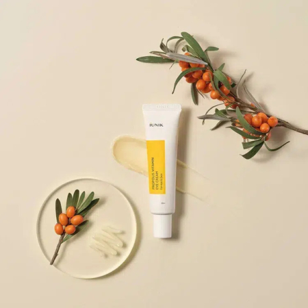 Un tube de crème contour des yeux vitaminée à la propolis iUNIK est posé sur une surface beige clair. Il est accompagné d'une petite branche garnie de baies et de feuilles, d'une touche de crème et d'un récipient transparent contenant les mêmes baies et feuilles. Dakar