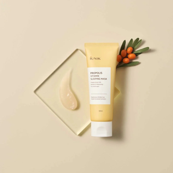 Un tube de masque de nuit vitaminé à la propolis iUNIK est placé sur un fond beige. À côté, une couche de produit est appliquée sur un carré de verre et de petits fruits orange aux feuilles vertes. Dakar