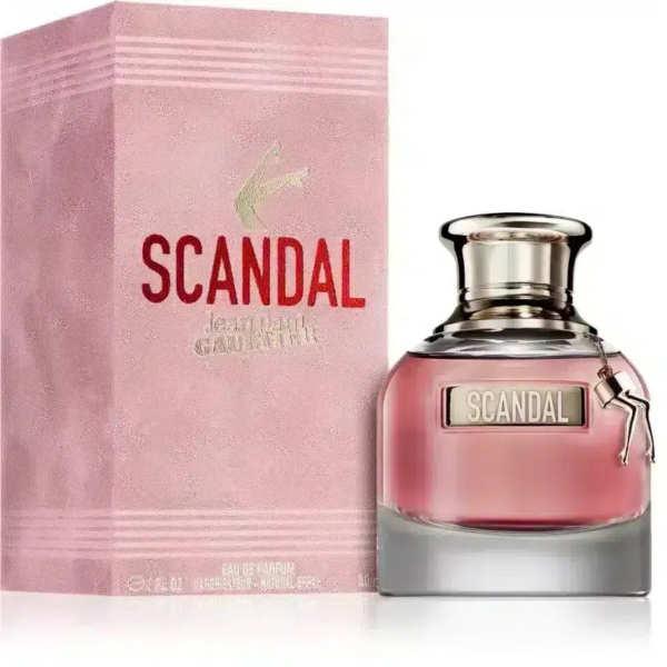 Un flacon de parfum Scandal, avec une base rose dégradée et un bouchon argenté, est présenté dans son coffret rose assorti. Le coffret porte l'inscription « SCANDAL » en lettres rouges et grasses. Le flacon est orné d'une petite breloque en forme de jambe. Dakar