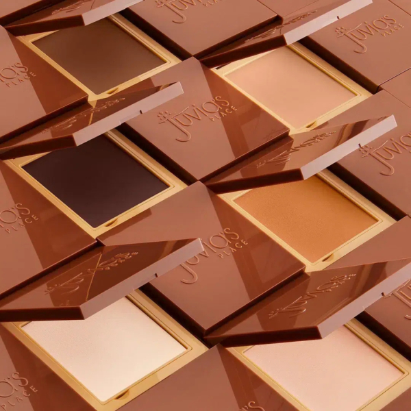 Une collection de poudriers de maquillage marron et beige de Juvia's Place, présentés en diagonale. Chaque poudrier, légèrement ouvert, dévoile une gamme de poudres aux teintes claires et foncées. Le logo de la marque est visible sur l'emballage. Dakar