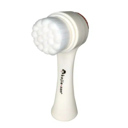 Une brosse nettoyante visage blanche dotée d'une tête texturée et d'un manche orné du logo et du texte « kojie∙san ». La tête est dotée de plusieurs poils doux conçus pour les soins de la peau. Dakar
