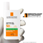 Gros plan d'une main gantée tenant un flacon de crème solaire La Roche-Posay Anthelios UVMUNE 400. Le flacon, doté d'un indice de protection solaire SPF 50+, est présenté comme un fluide anti-sébum offrant une protection UVA ultra-longue durée. Le texte indique qu'il s'agit de la marque la plus recommandée par les dermatologues au Royaume-Uni. Dakar