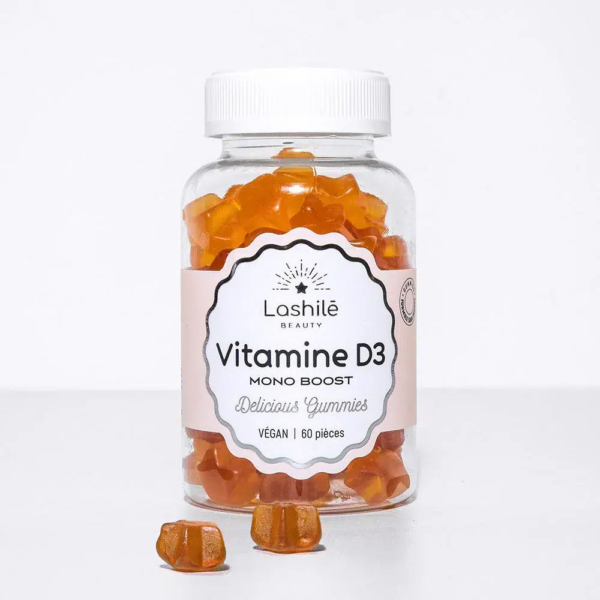 Une bouteille en plastique transparent étiquetée « Lashilé Beauty Vitamine D3 Mono Boost » contient des compléments alimentaires gélifiés orange. L'étiquette mentionne « Délicieux gélifiés », « Vegan » et « 60 pièces ». Quelques gélifiés sont dispersés devant la bouteille. Dakar