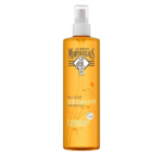 Un grand flacon vaporisateur orange contenant l'Huile Sèche Sublimante Le Petit Marseillais au beurre de karité, à l'amande douce et à l'huile d'argan. L'étiquette arbore un petit emblème noir et divers détails du produit en français. Dakar