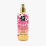 Un flacon de brume corps et cheveux sans alcool « Les Petits Plaisirs ». L'étiquette est rose avec des motifs de fleurs de cerisier et des touches dorées. Ce produit, appelé « Fleur de Cerisier », est fabriqué en France. Dakar