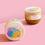 Deux pots de soins capillaires « Tropical Detox » aux couleurs pastel sur fond rose. L'un est vertical, l'autre incliné sur le côté, affichant des étiquettes et du texte colorés. Les ombres projetées par les pots sont visibles en arrière-plan. Dakar