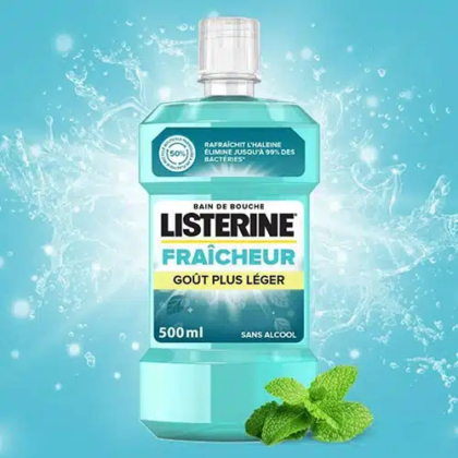 Un flacon de bain de bouche Listerine de 500 ml portant l'inscription « FRAÎCHEUR GOÛT PLUS LÉGER SANS ALCOOL ». Le liquide mentholé est mis en valeur sur un fond éclaboussé, avec des feuilles de menthe en bas à droite, soulignant la fraîcheur. Dakar