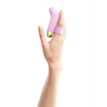 Une main à la peau claire est représentée avec un petit vibromasseur rose à base dorée. Le jouet est fixé au majeur par une sangle. Le fond est blanc uni. Dakar