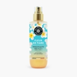 Un flacon spray de 200 ml de "Les Petits Plaisirs Brume Pailletée Fleur de Tiaré" présente un design tropical avec des fleurs blanches et jaunes, étiqueté comme une brume corps et cheveux sans alcool, fabriquée en France. Dakar