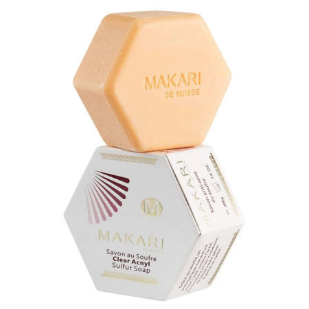 Barre hexagonale de savon transparent au soufre et à l'acétate Makari de Suisse, orange, posée sur sa boîte. La boîte est blanche avec des inscriptions et des motifs dorés et marron. Dakar