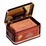 Un pain de savon exfoliant rectangulaire, étiqueté « Makari Exclusif », est présenté dans une boîte métallique à charnière aux accents marron et doré. Le texte sur la boîte souligne ses propriétés exfoliantes et éclaircissantes. Dakar