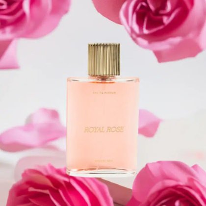 Un flacon de parfum rose, étiqueté « Royal Rose », avec un bouchon doré, est placé au milieu de pétales et de fleurs d'un rose tendre. L'arrière-plan est flou, créant une atmosphère romantique et élégante. Dakar