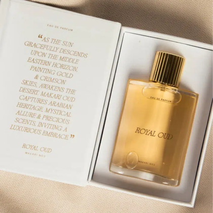 Un flacon de parfum « Royal Oud » au bouchon doré est présenté dans un coffret ouvert. Ce coffret présente une description poétique de la fragrance, mettant en valeur les thèmes du luxe et du mystère arabe. Le texte est écrit dans une élégante police dorée. Dakar