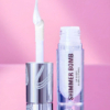 Un tube de gloss transparent et scintillant, doté d'un applicateur blanc brillant, est ouvert sur un fond rose. L'inscription « SHIMMER BOMB » est inscrite en gras. L'emballage arbore un design métallique élégant. Dakar