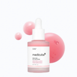 Un flacon de sérum aux peptides roses pour les pores de Medicube, muni d'un bouchon compte-gouttes, est mis en valeur. L'arrière-plan présente trois sphères roses de tailles différentes, qui complètent les touches de rose du produit. L'étiquette présente les informations sur le produit et la marque. Dakar