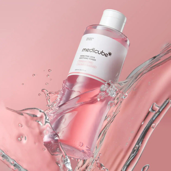 Un flacon transparent de lotion tonique tonifiante Medicube Pore PHA 2.0 au liquide rose est orné d'une éclaboussure dynamique sur fond rose. L'étiquette du flacon est principalement blanche avec du texte gris et rose. Dakar