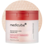 Un pot de disques exfoliants Medicube à l'acide succinique rouge avec un couvercle rouge. L'étiquette indique : acide succinique 0,5 %, panthénol 0,5 % et niacinamide 2 %. Le pot contient 70 disques et pèse 155 g. Dakar