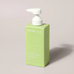 Bouteille rectangulaire verte avec une pompe blanche, étiquetée « MEDIX 5.5 » et « Crème pour le corps à l'huile de coco + miel de Manuka, régénérante et régénérante, 15 oz liq. (443 ml). Dakar
