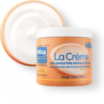 Pot de Mixa La Crème, sans couvercle, à la texture onctueuse. Le contenant orange est orné d'un texte en français, soulignant son utilisation pour les peaux très sèches, avec des beurres de cacao et de karité. Convient pour le visage, le corps et les mains. Dakar